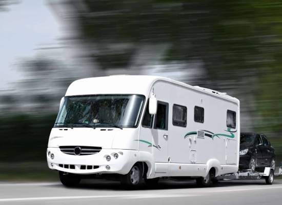 RV traveling down a highway towing an automobile behind