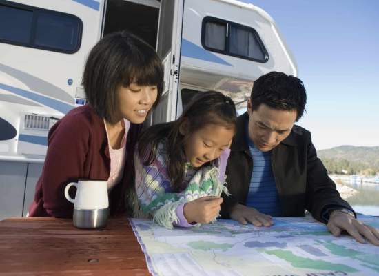 Parents and daughter outside their RV, looking at a map 